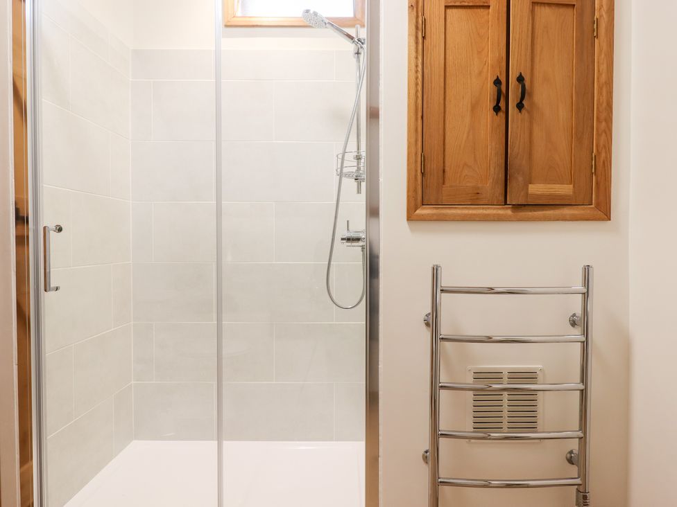 A shower area with glass door a handheld shower head wooden cabinet above a chrome towel rail