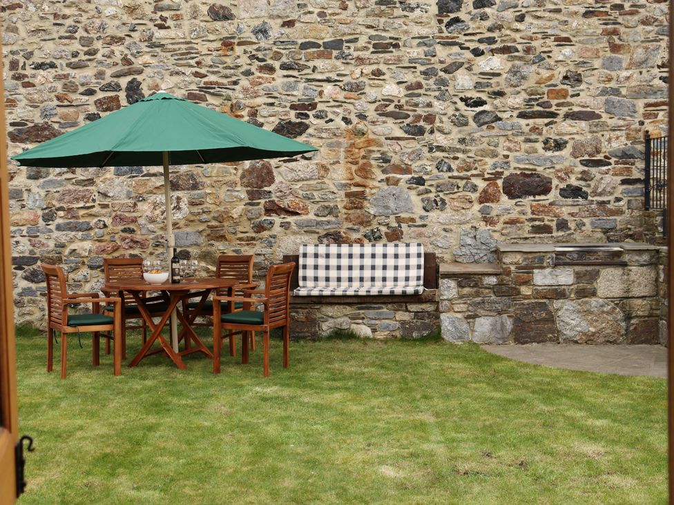 An outdoor seating area with wooden table and chairs under a green umbrella and a stone bench with cushion at Little Orchard in Ashburton Down near Ashburton