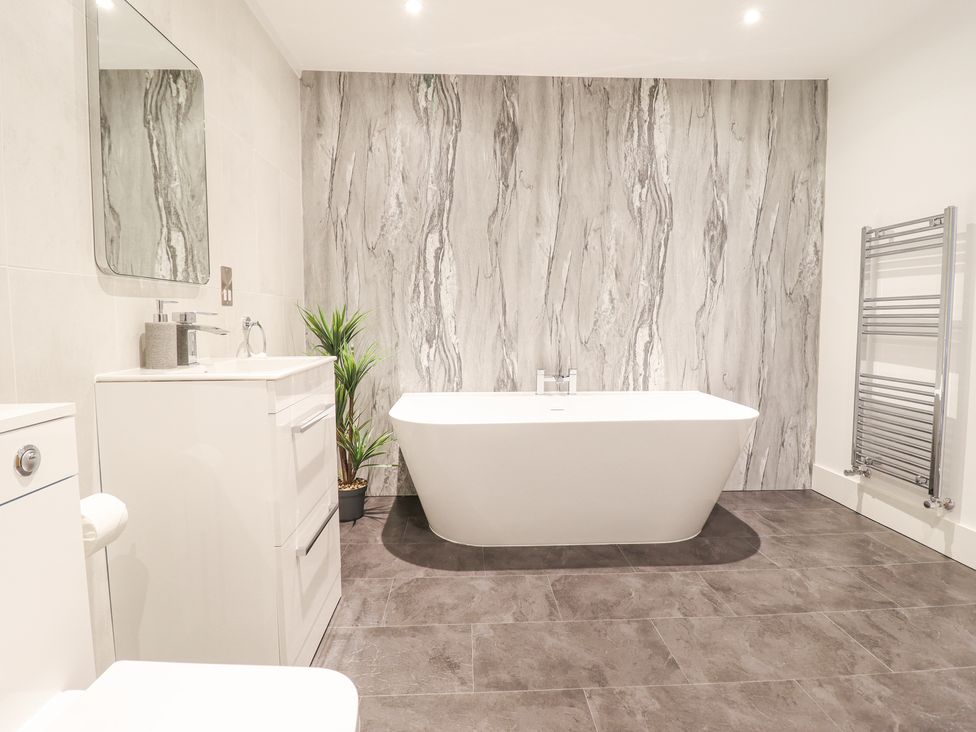 A bathroom with a white freestanding bathtub a sink with a mirror a toilet a plant and a towel radiator at Aelfor in Harlech