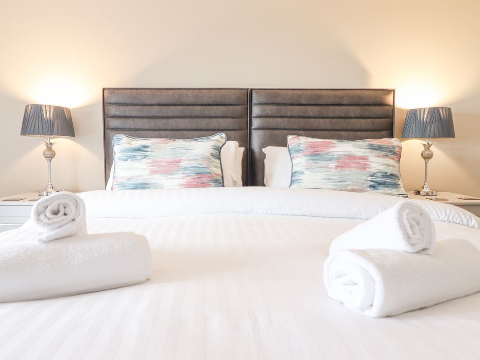 A bed with a headboard two patterned pillows two bedside tables with lamps and rolled white towels on the bed at Aelfor in Harlech
