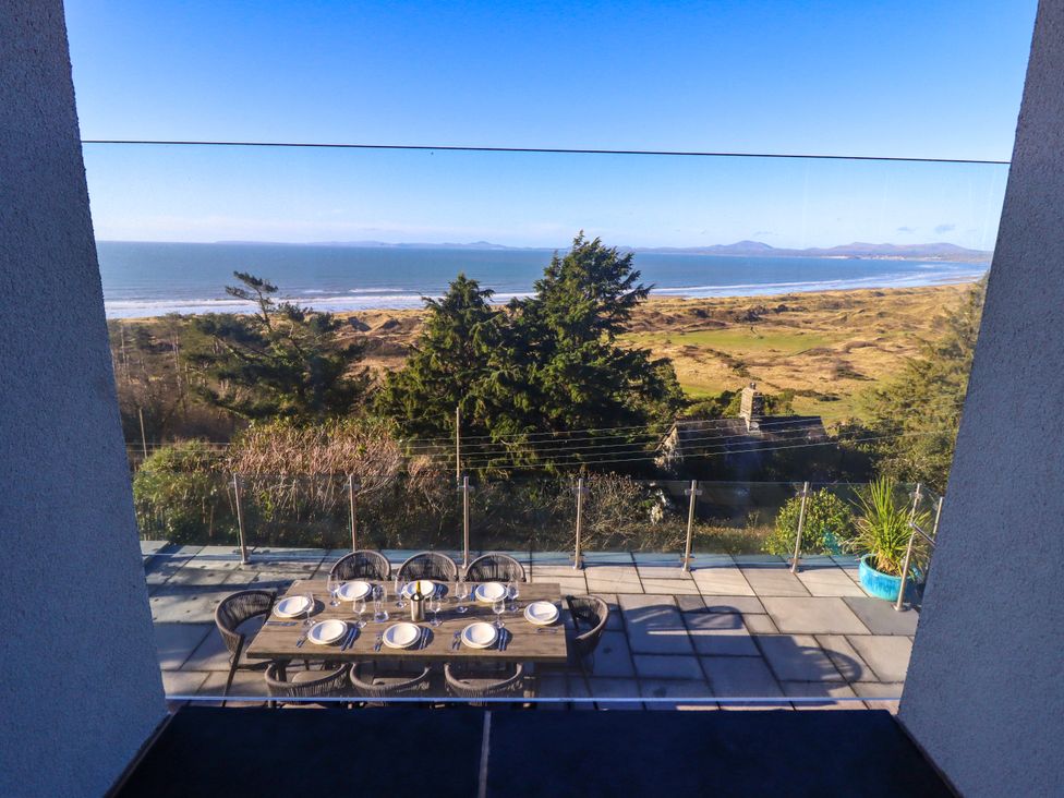 An outdoor dining table set for eight on a balcony overlooking trees sand dunes and the ocean at Aelfor in Harlech