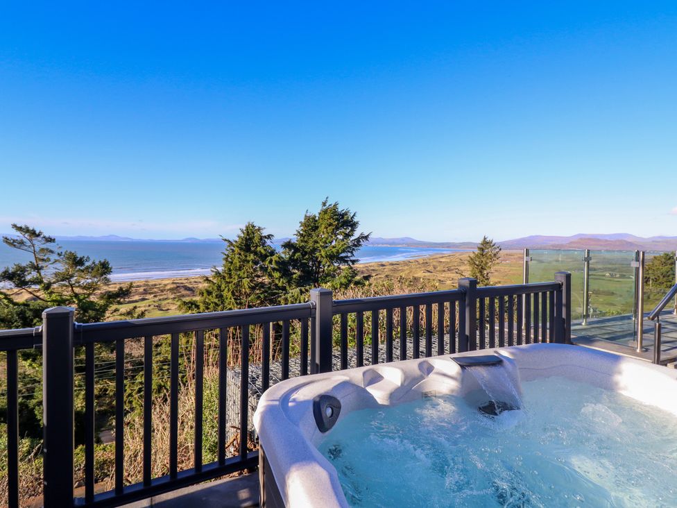 An outdoor hot tub on a deck overlooking trees a beach and the ocean at Aelfor in Harlech