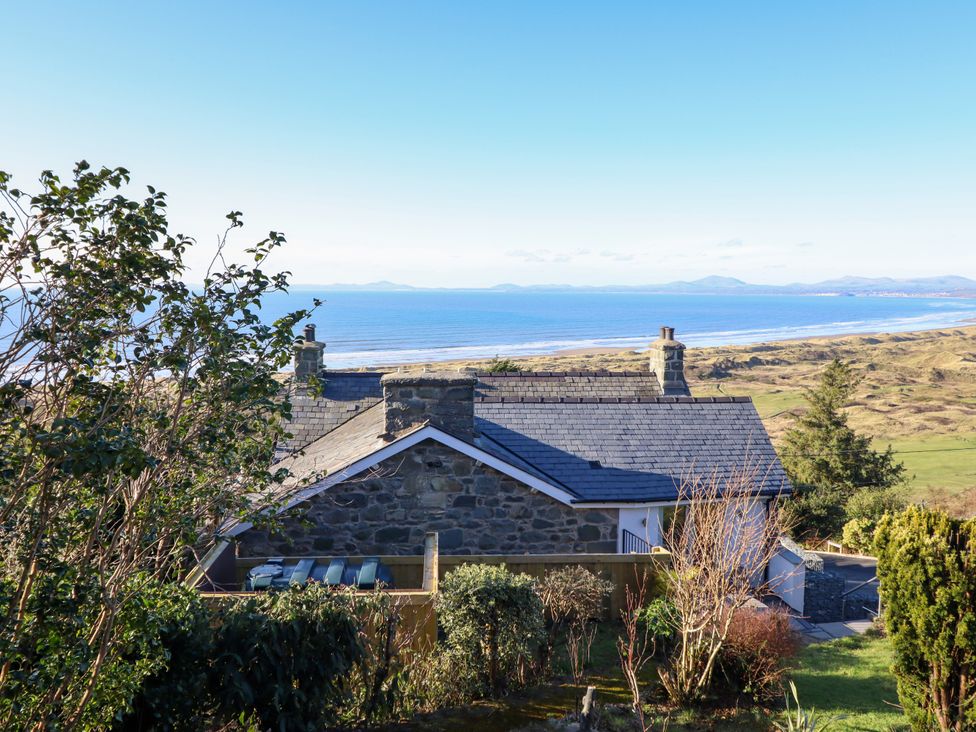 A stone house with chimneys near the sea with hills in the background at Aelfor in Harlech