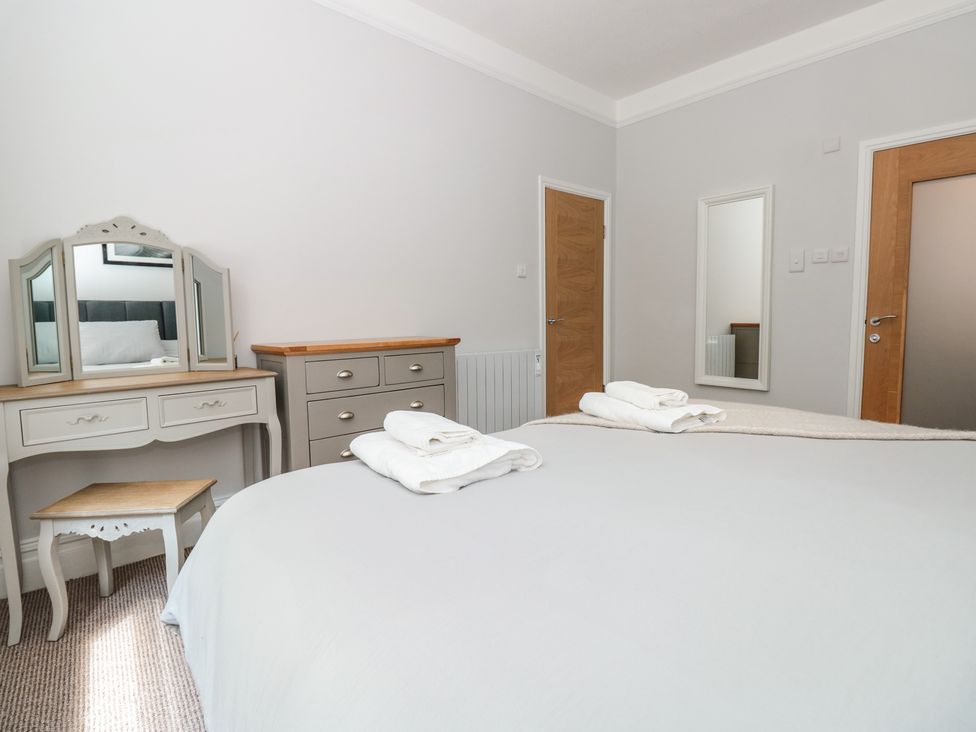 A bedroom with a bed, two sets of folded towels, a dresser with a mirror, a chest of drawers, a stool, two wooden doors, and a wall mirror at Flat 1 Byfield in Torquay