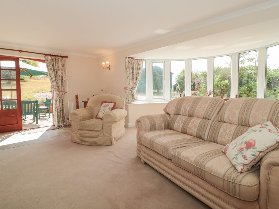 A living room with a sofa and armchair near bay windows and a door leading to an outdoor seating area at Rhode Acres in Fifehead Neville near Hazelbury Bryan