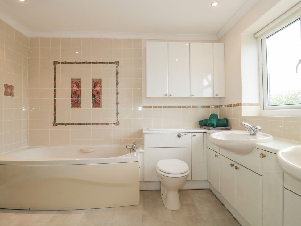 A bathroom with a bathtub a toilet two sinks cabinets and a window at Rhode Acres in Fifehead Neville near Hazelbury Bryan