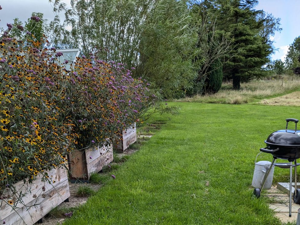 A garden with wooden flower boxes full of plants and a barbecue grill on a lawn at Rhode Acres in Fifehead Neville near Hazelbury Bryan