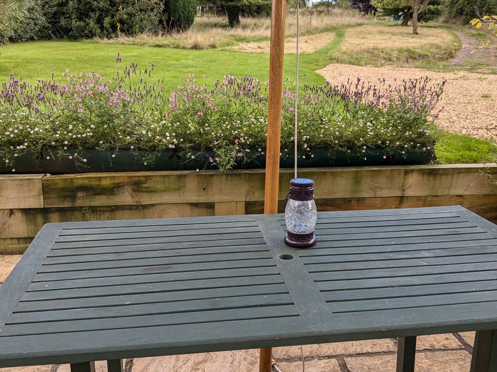 A wooden outdoor table with a lantern on it and a garden with grass flowers and a gravel path at Rhode Acres in Fifehead Neville near Hazelbury Bryan