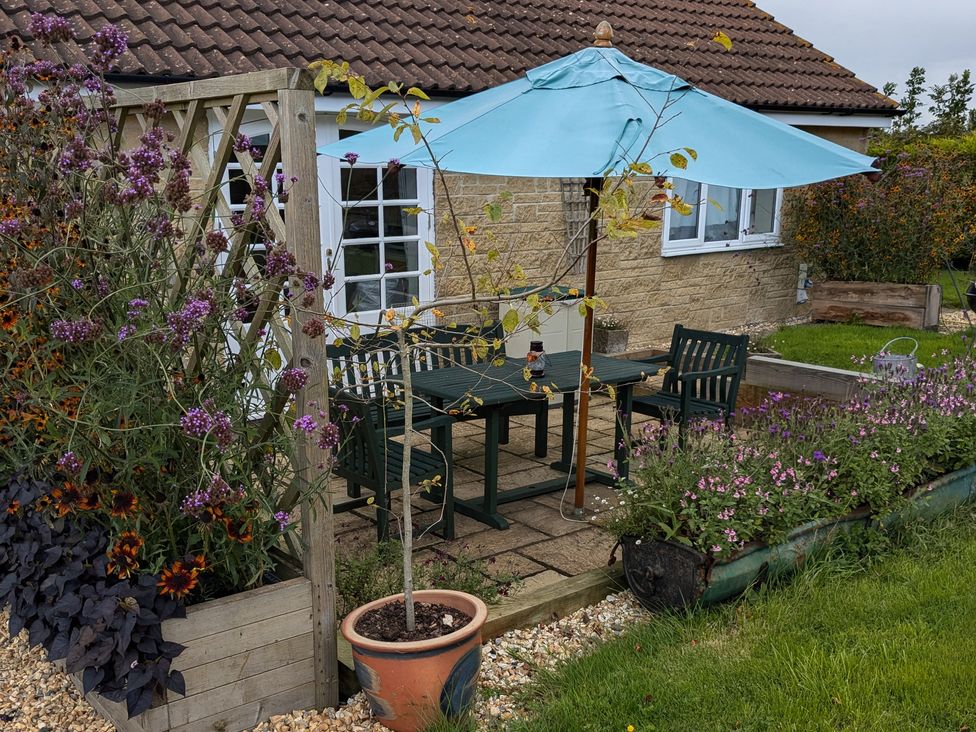 A garden patio with a table, chairs, a blue umbrella, potted plants, and flowers at Rhode Acres in Fifehead Neville near Hazelbury Bryan