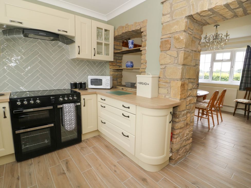A kitchen with a stove, microwave, and bread box next to a stone archway leading to a dining area at 2 Crosslands in Stockton-On-The-Forest