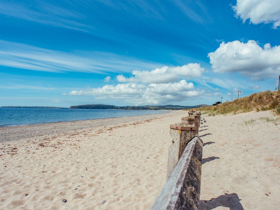 A sandy beach with wooden fence posts leading towards grassy dunes and a blue sky with clouds at Hen Felin in Llangybi near Pwllheli