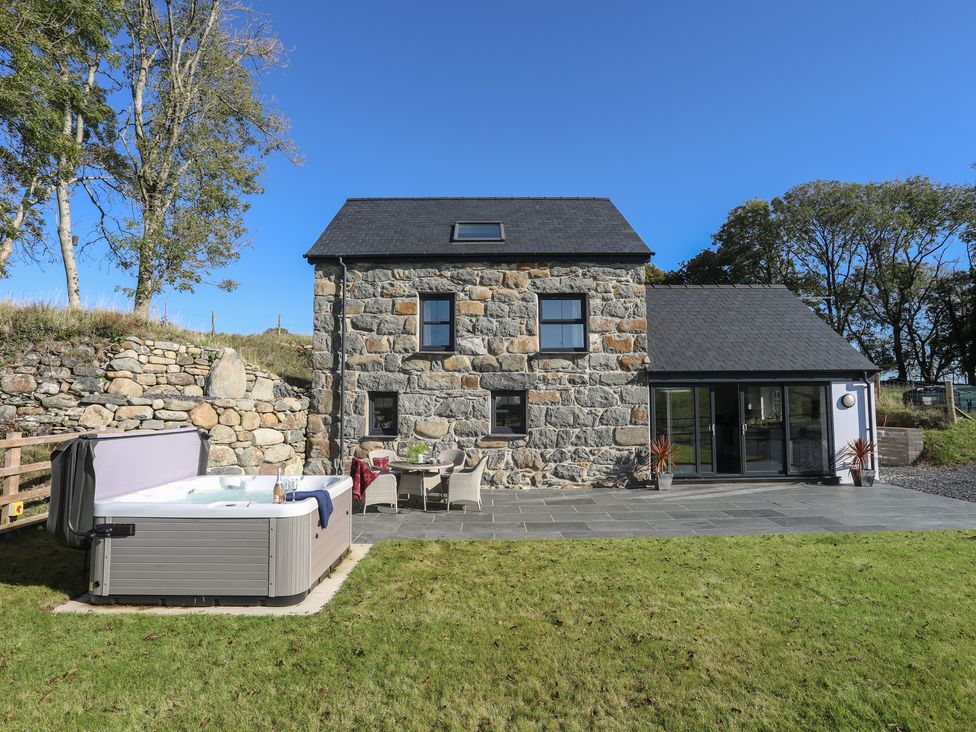 A stone house with a patio table and chairs and a hot tub in the garden at Hen Felin in Llangybi near Pwllheli