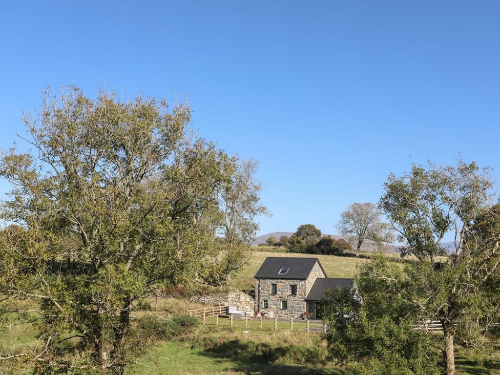 A stone house with outdoor furniture in a fenced yard surrounded by trees in a rural area at Hen Felin in Llangybi near Pwllheli