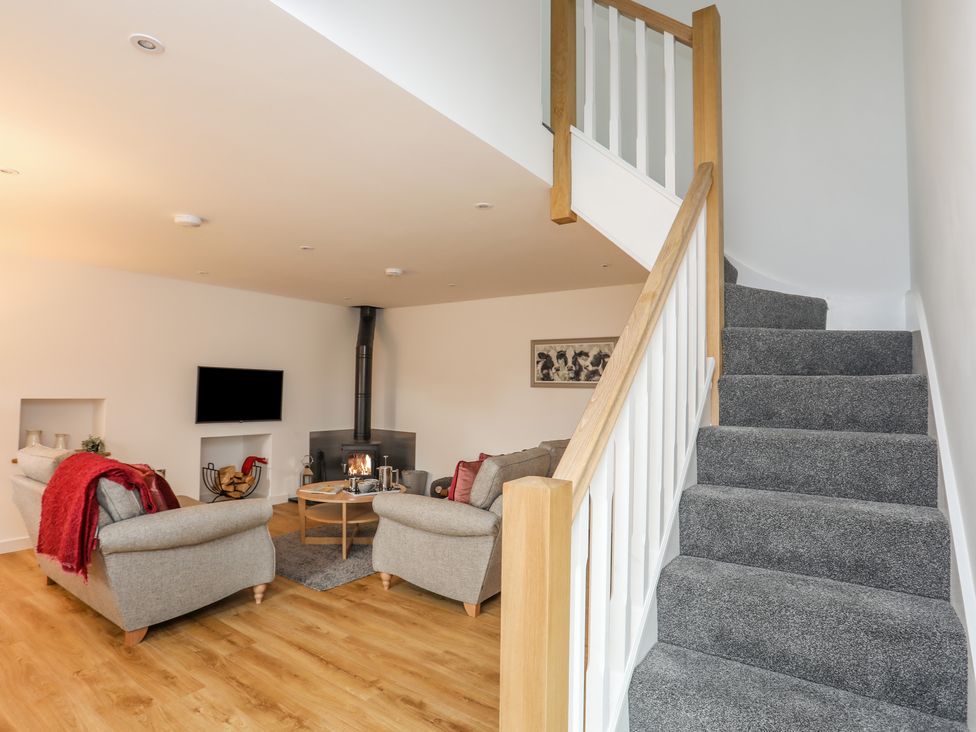 A living room with two sofas a round coffee table a wood burning stove and gray carpeted stairs at Hen Felin in Llangybi near Pwllheli