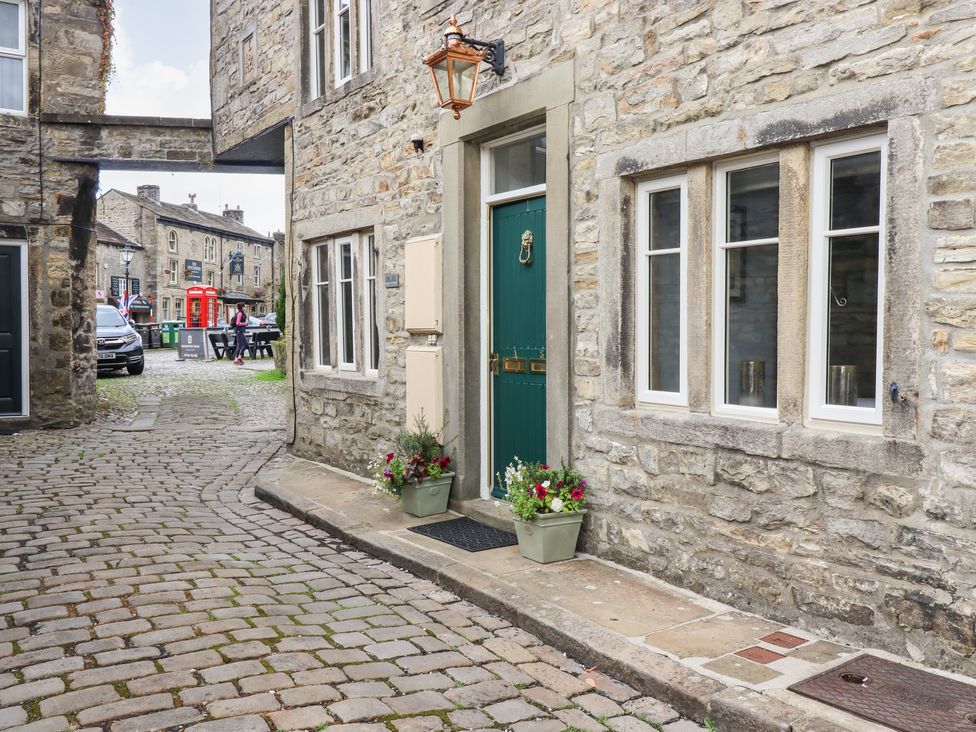A cobblestone street with a stone building featuring a green door and three windows at Squint Cottage in Grassington