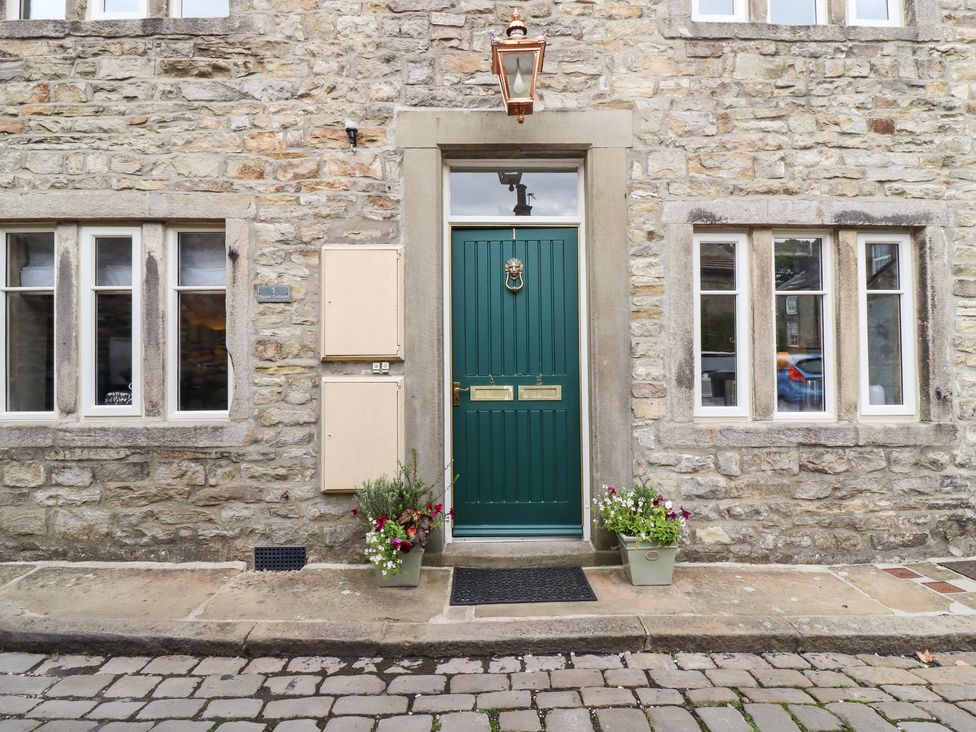 A front entrance with a green door and two flower pots on a cobblestone street at Squint Cottage in Grassington