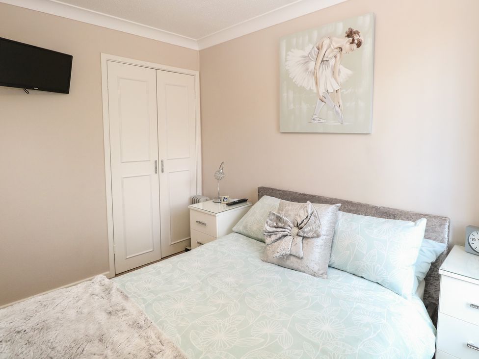 A bedroom with a bed lamps bedside tables a wall-mounted TV and a ballerina painting at 30 The Waterside Holiday Park in Corton