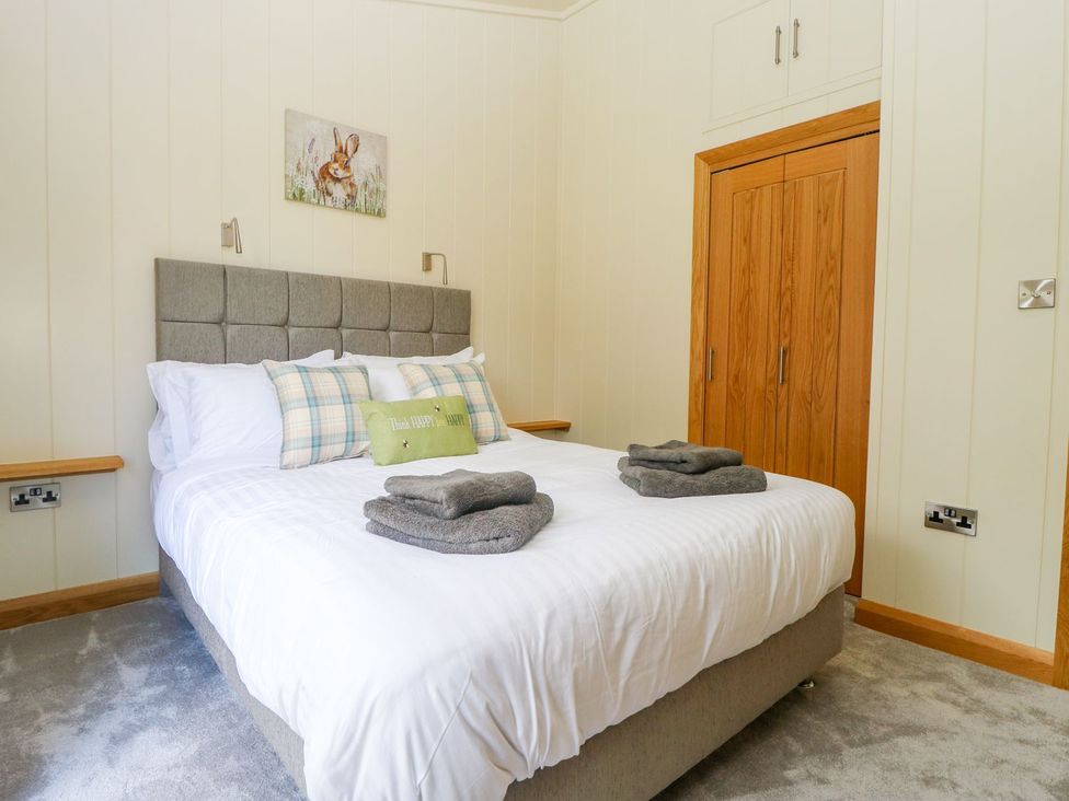 A bedroom with a double bed with gray headboard pillows and folded towels at Robin Lodge in Gargrave
