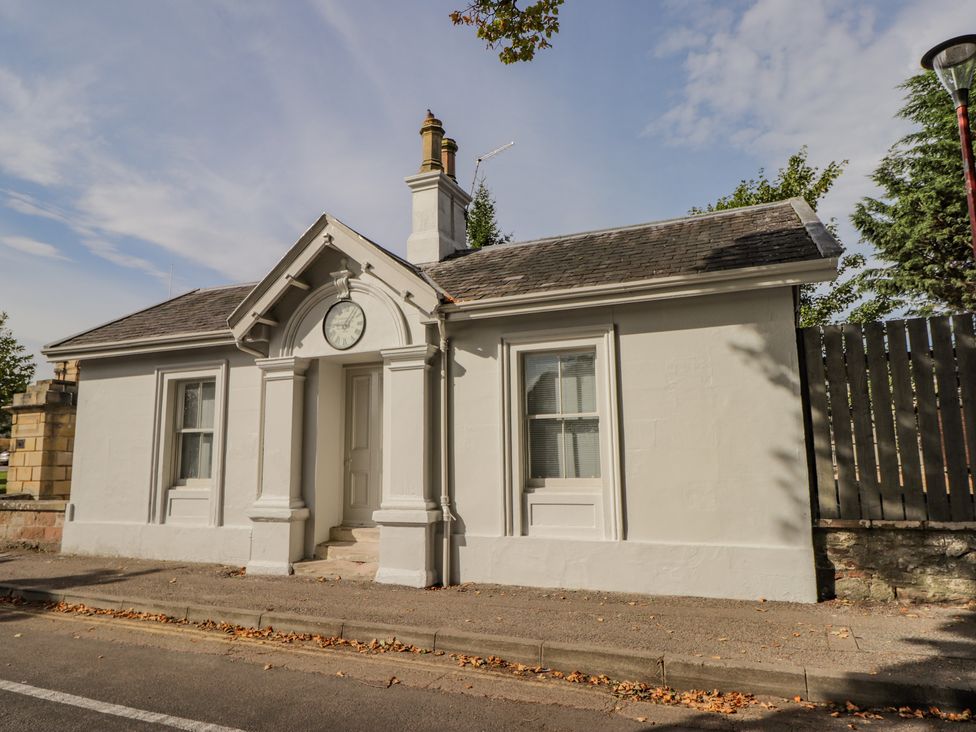 A small white building with a clock above the door next to a sidewalk and street at Porter's Lodge in Inverness