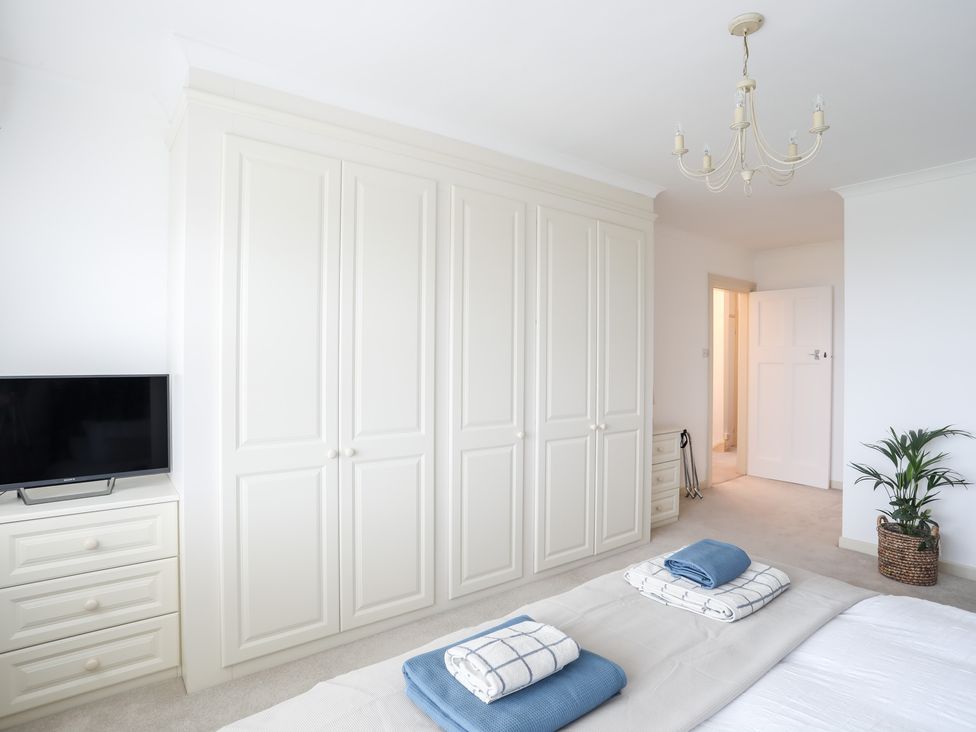 A bedroom with white wardrobes a television on a dresser and folded towels on a bed at Awelfryn in Criccieth