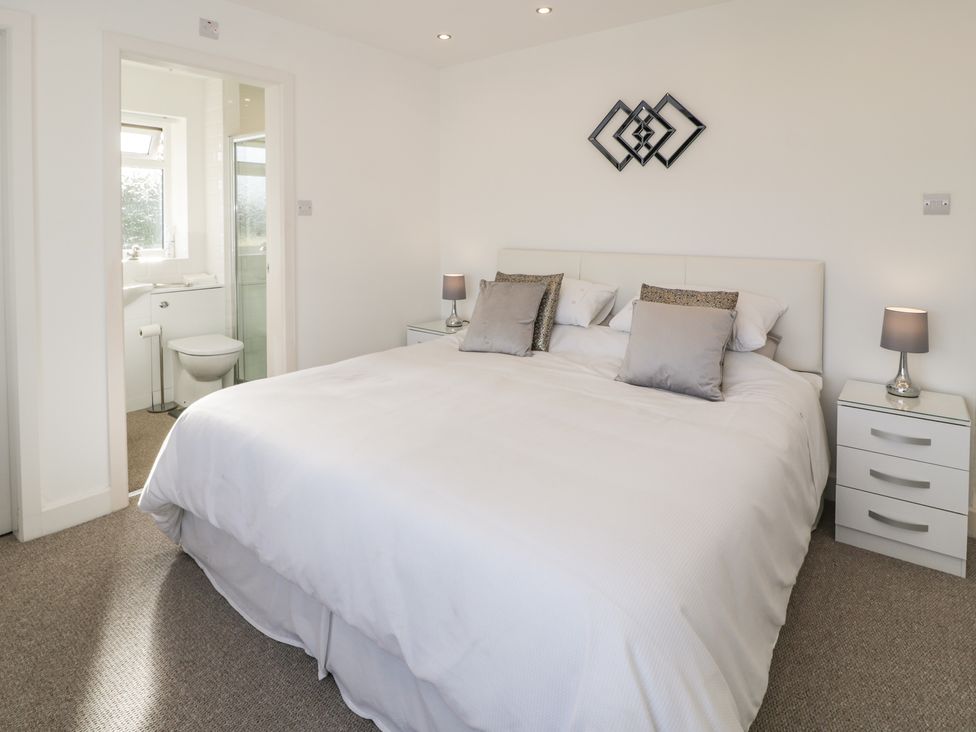 A bedroom with a large bed and bedside tables with lamps and an en suite bathroom at Top Of The Lane Luxury Holiday Apartment in Benllech