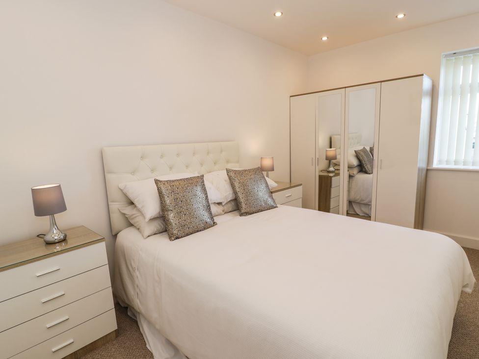 A bedroom with a bed, bedside tables with lamps, a wardrobe with mirrored doors, and a window at Top Of The Lane Luxury Holiday Apartment in Benllech