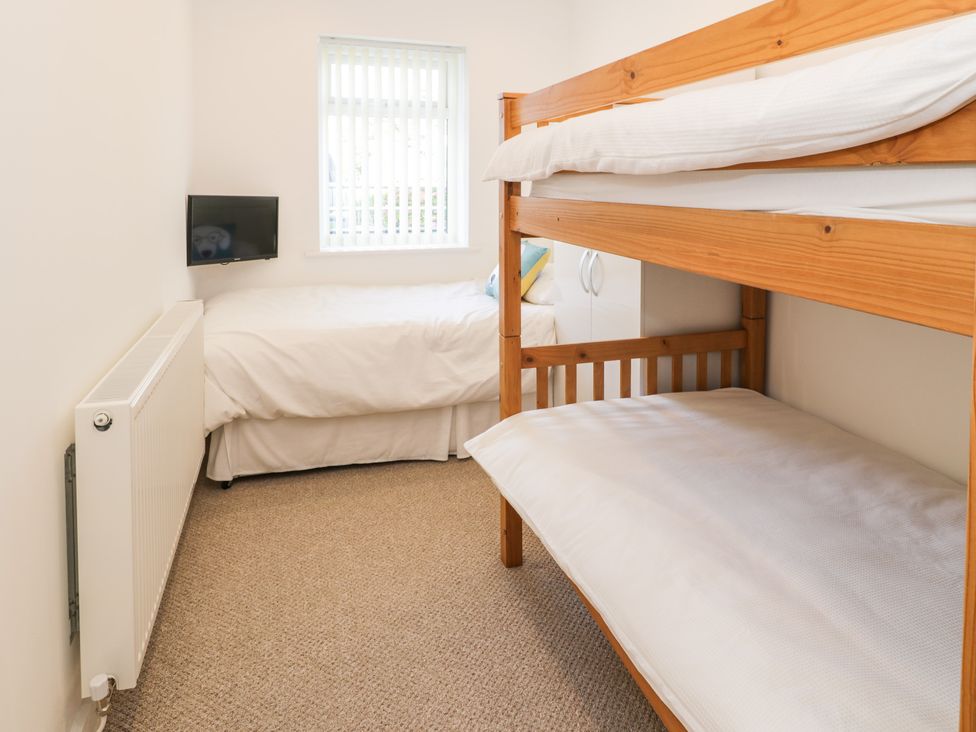 A bedroom with a bunk bed and a single bed with a TV mounted on the wall at Top Of The Lane Luxury Holiday Apartment in Benllech