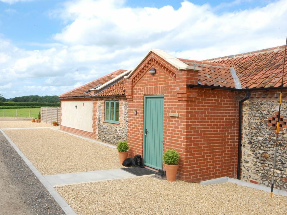 A brick and flint house with a green door with two potted plants and a black dog lying on a mat at Remus in Larling near East Harling