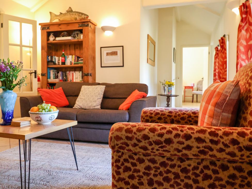 A living room with a sofa, armchair, coffee table with fruit bowl and flowers, wooden cabinet with books and a fish decoration at Remus Larling near East Harling