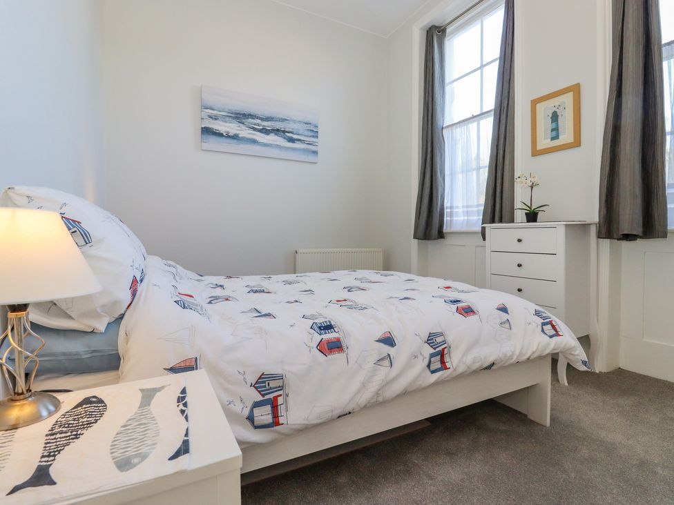 A bedroom with a bed a bedside table with lamp and a dresser near windows at The Old Spy Headquarters in Folkestone