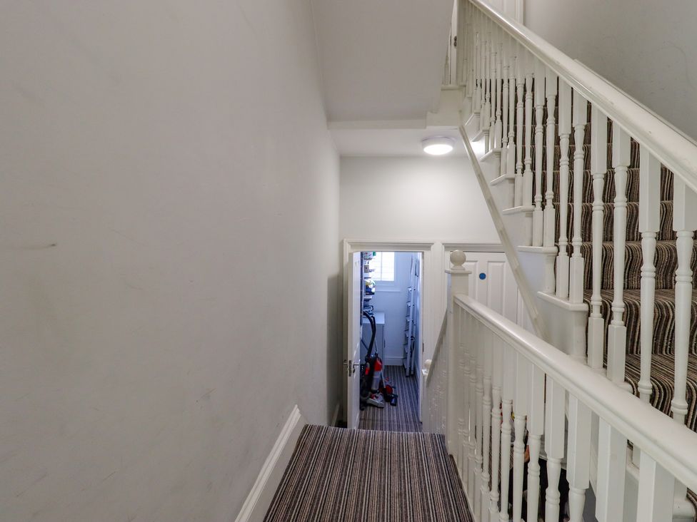 A staircase with striped carpet and white railings leading to a lower hallway with cleaning equipment at The Old Spy Headquarters in Folkestone