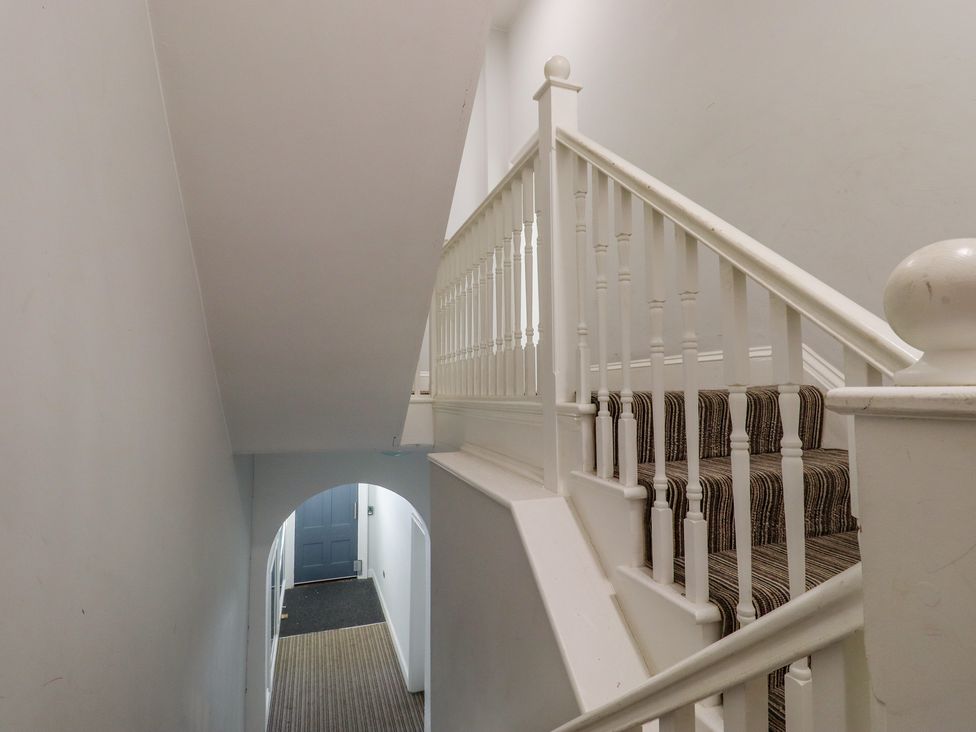 A stairway with striped carpet and white railing leading down to a hallway with an arched doorway at The Old Spy Headquarters in Folkestone