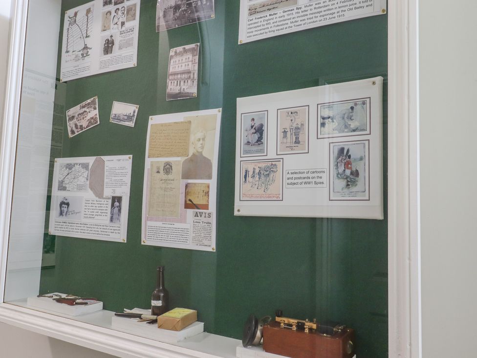 A museum display case with historical photographs documents and small artifacts on a green background at The Old Spy Headquarters in Folkestone