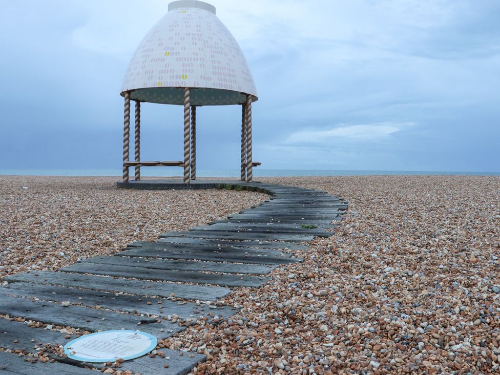 A pebble beach with a winding wooden pathway leading to a small shelter with a dome roof and twisted columns at The Old Spy Headquarters in Folkestone