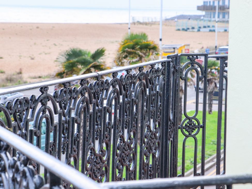A balcony with ornate black metal railing overlooking palm trees a beach and buildings at The Old Spy Headquarters in Folkestone