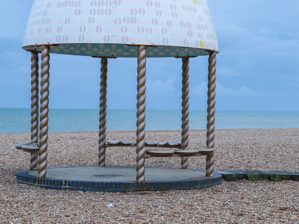A beach shelter with twisted columns and built-in seating on a pebble beach with the sea and sky in the background at The Old Spy Headquarters in Folkestone
