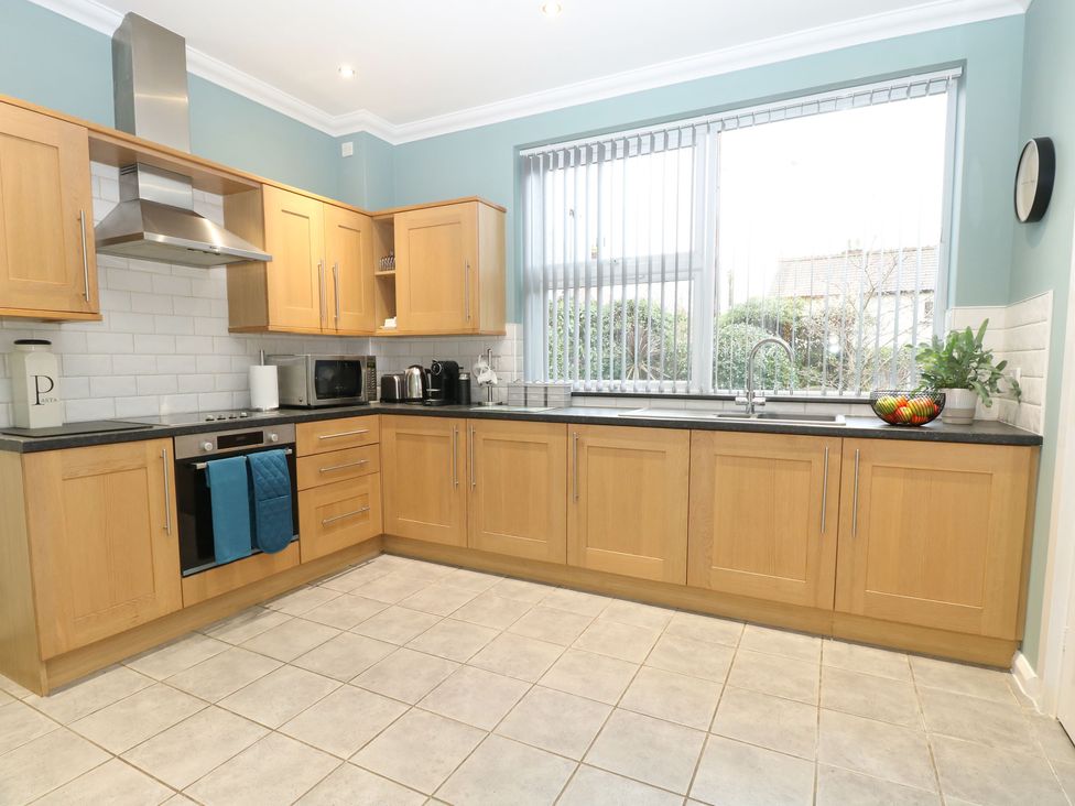 A kitchen with wooden cabinets a stove oven and microwave next to a large window with vertical blinds at Brundall House in Brundall
