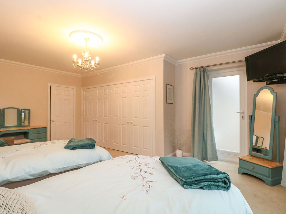 A bedroom with two beds, a vanity desk, a full-length mirror, closets, and a door with a curtain at Brundall House in Brundall