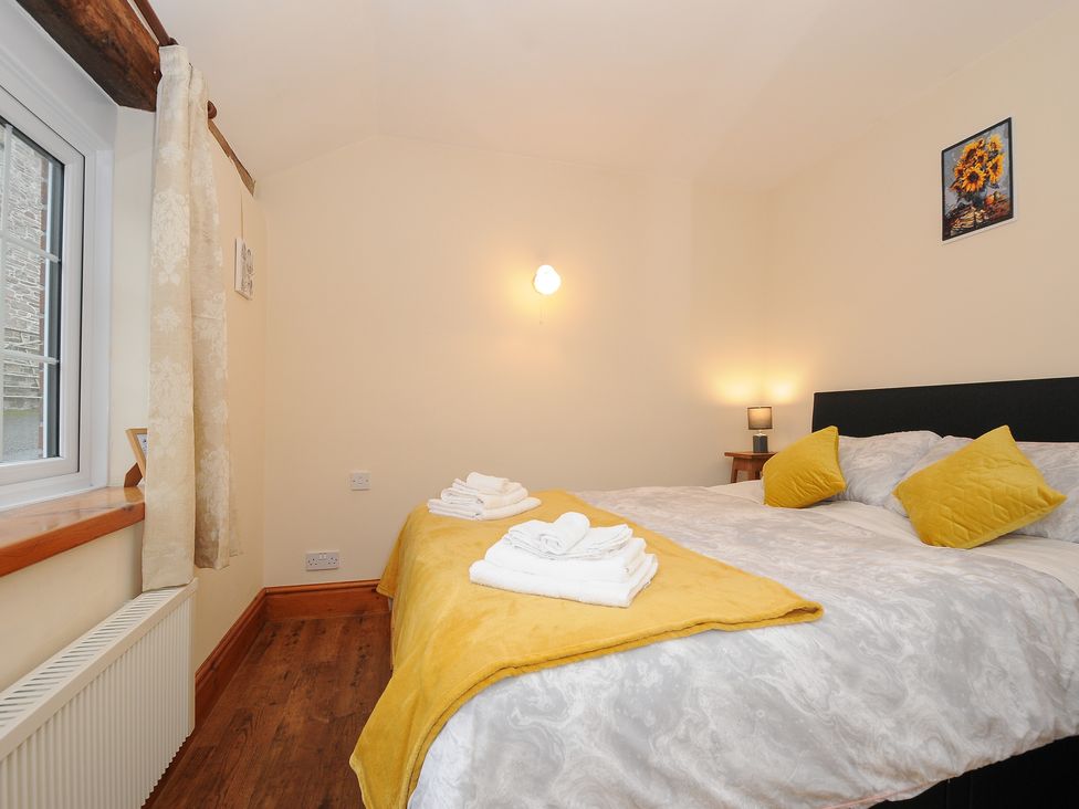 A bedroom with a double bed yellow pillows and blanket a window with curtains and a framed picture on the wall at The Wagon House in Lezant near Launceston