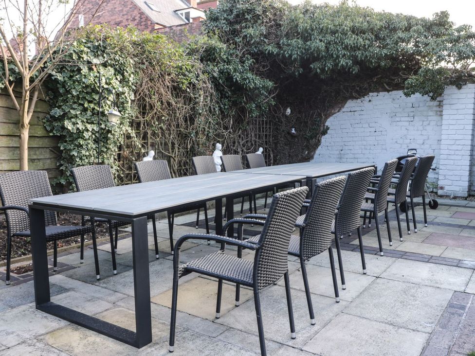An outdoor seating area with a long table and chairs on a patio with plants and a white brick wall at Wellington House in Bridlington