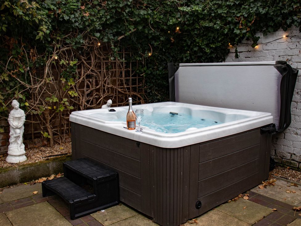 An outdoor hot tub with steps surrounded by ivy-covered walls and a statue with a bottle and glass on the edge of the tub at Wellington House in Bridlington