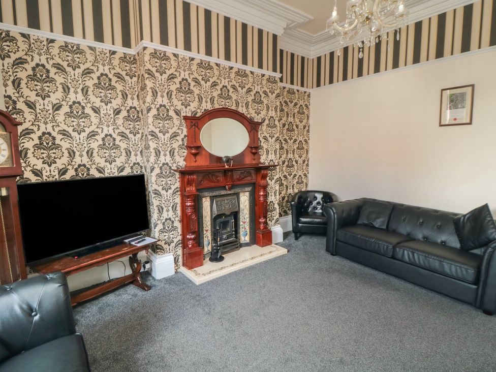 A living room with a fireplace a television on a wooden stand a black leather sofa and armchair at Wellington House in Bridlington
