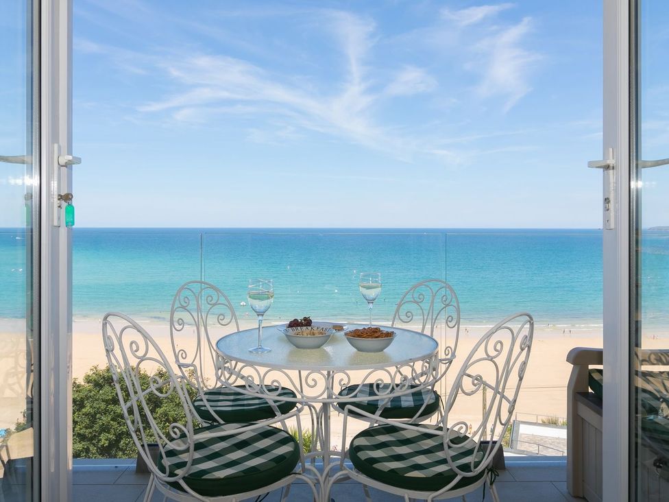 A balcony with a round table and four chairs overlooking the beach and ocean at Surf and Sand in Carbis Bay