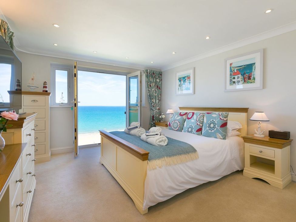 A bedroom with a bed facing an open door to the sea at Surf and Sand in Carbis Bay