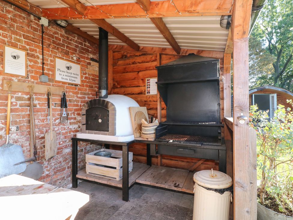 An outdoor cooking area with a brick oven and a black barbecue grill next to gardening tools hanging on a brick wall at Elm in Rocester