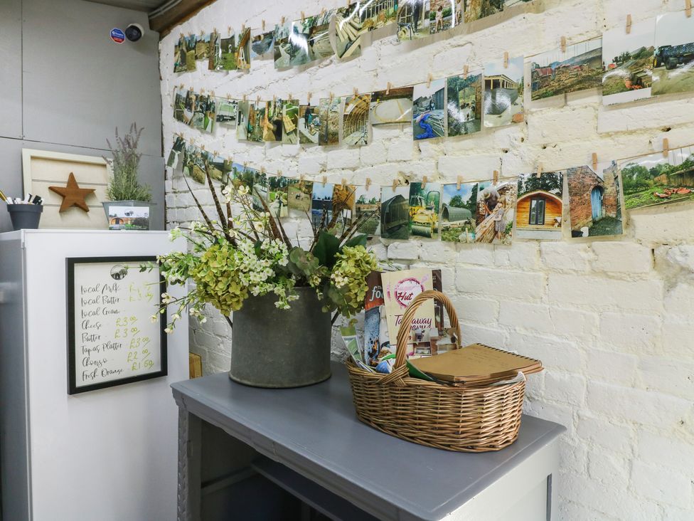 A corner of a room with a grey table holding a flower arrangement and a wicker basket next to a wall with photos clipped on strings at Elm in Rocester