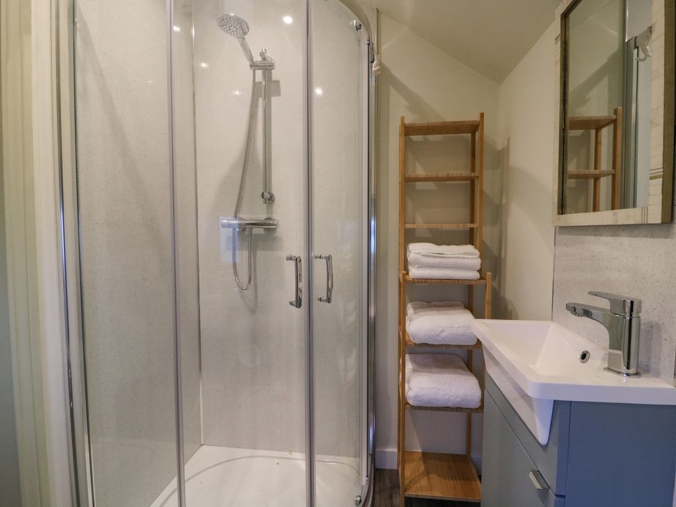A bathroom with a glass shower enclosure a wooden shelf with towels and a sink with a faucet at Pheasant in Bedale
