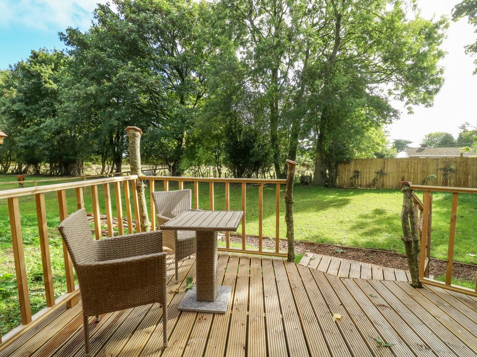 A wooden deck with two wicker chairs and a table overlooking a grassy backyard with trees and a wooden fence at Pheasant in Bedale
