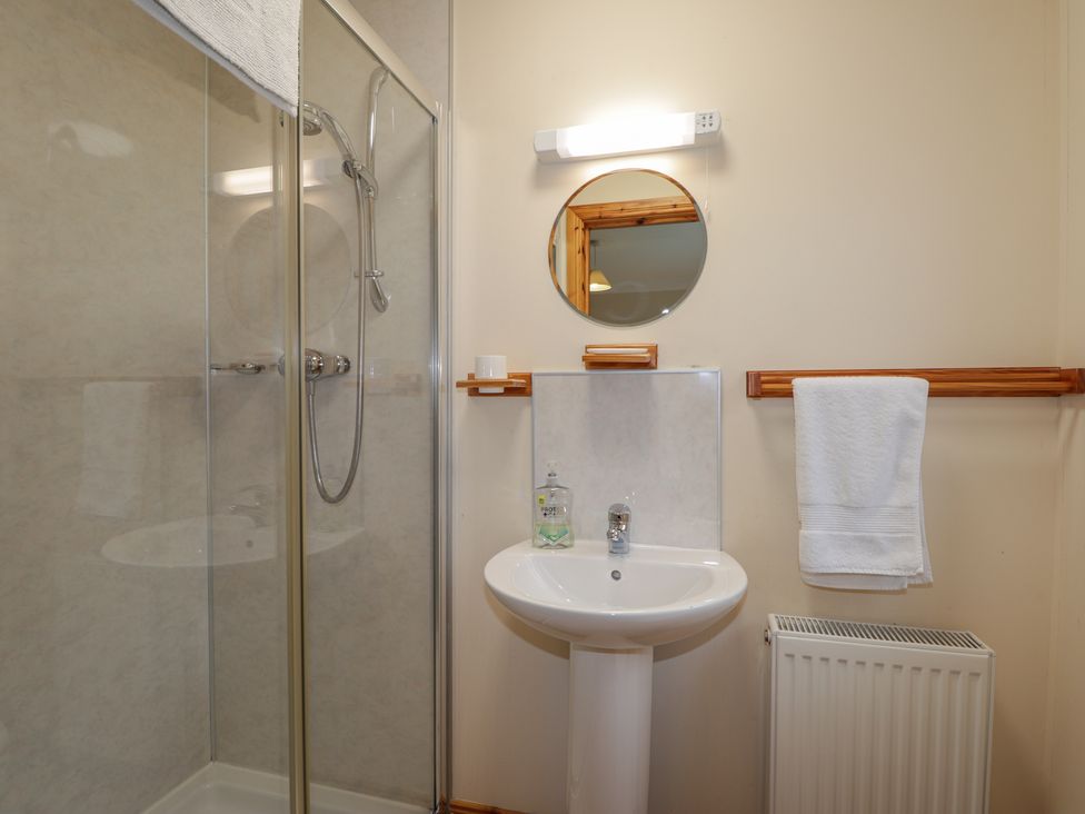 A bathroom with a shower enclosure sink round mirror towel radiator and soap dispenser at Tigh na Drochit in Eilanreach near Glenelg