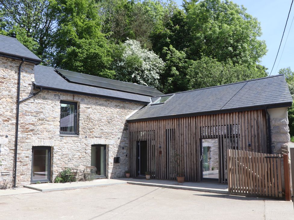 A stone and wood house exterior with solar panels on the roof and potted plants near the entrance at 3 Caddaford Barns in Buckfastleigh